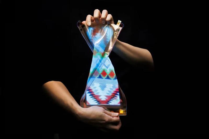 Disembodied hands twist a flexible screen with a colorful display against a black backdrop.